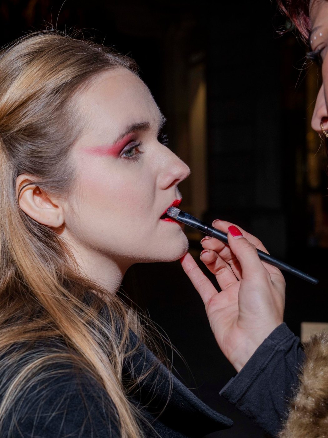 Makeup artist applying red lipstick backstage